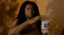 a shirtless man with dreadlocks is holding a jar of cream in his hand .