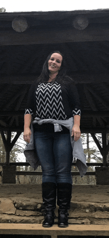 a woman wearing a black and white chevron shirt and black boots stands under a gazebo