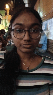 a young woman wearing glasses and a necklace looks at the camera