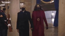 obama and michelle obama are holding hands while walking down a hallway .