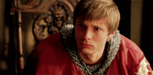 a young man wearing a red jacket with chain mail around his neck