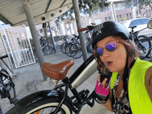 a woman wearing sunglasses and a helmet with the letter j on it stands next to a bicycle