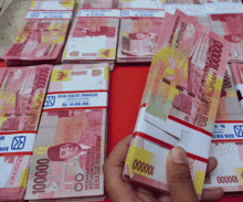 a hand is holding a stack of 100000 rupiah bills