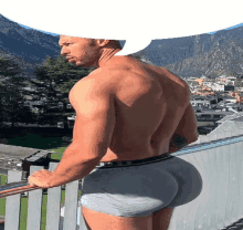 a shirtless man in boxer shorts is standing on a balcony with a large butt .