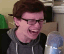 a young man wearing glasses and a hoodie is laughing in front of a microphone .