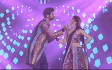 a man and a woman are dancing on a stage with purple lights behind them .