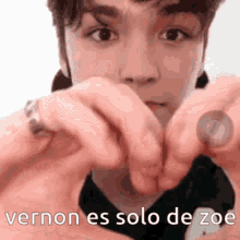 a young man is making a heart with his hands with the words vernon es solo de zoe written below him