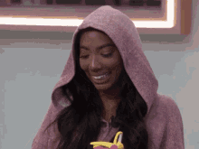 a woman wearing a pink hoodie is smiling and holding a toy