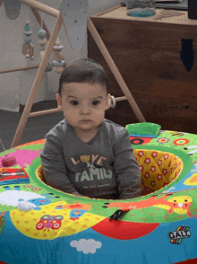 a baby wearing a shirt that says love family sits in a colorful play mat