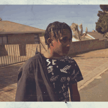 a young man wearing a black shirt with graffiti on it is walking down the street