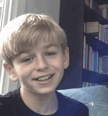 a young boy in a black shirt smiles in front of a bookshelf