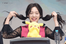 a girl with pigtails holds a stuffed pikachu