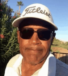 a man wearing sunglasses and a titleist hat