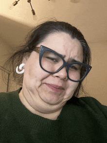 a woman wearing glasses and a green sweater is making a funny face