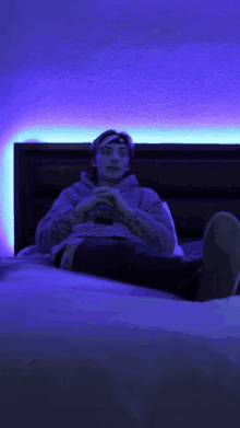 a young man is laying on a bed with a blue light behind him