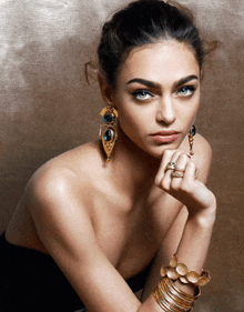 a woman wearing earrings and a ring is sitting with her hand on her chin