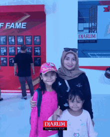 a woman and two little girls pose for a picture in front of a wall that says diarum badminton club