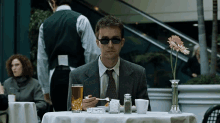 a man in a suit is sitting at a table with a glass of beer