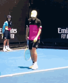 a man in a pink shirt is holding a tennis racquet on a tennis court with emirates in the background