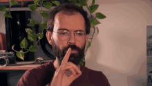 a man with glasses and a beard has his finger on his mouth