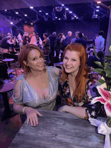 two women are sitting at a table in a crowded room