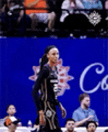 a female basketball player is walking on the court in front of a crowd .