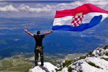 a man standing on top of a mountain holding a croatian flag