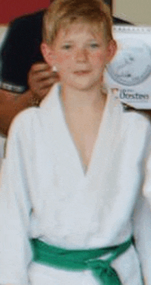 a young boy wearing a white robe and a green belt