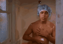 a shirtless man is taking a shower in a shower cap .