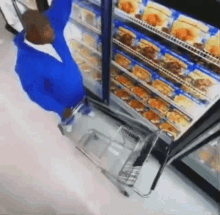 a man in a blue shirt is pushing a shopping cart in front of a refrigerator in a store .