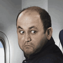 a bald man sitting on an airplane making a face