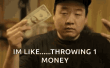 a man is holding a dollar bill in his hand and says `` im like throwing 1 money '' .