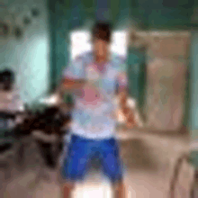 a man in a blue shirt and blue shorts is standing in a room with a blurred background .