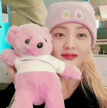 a woman wearing a purple beanie holds a pink teddy bear