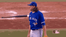 a man in a blue jays jersey is standing on a baseball field with a bat in the background .