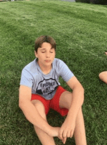 a young boy is sitting on the grass with his eyes closed and his legs crossed .