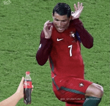 a person is holding a bottle of coca cola in front of a soccer player on the field .