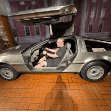 a man is sitting in a back to the future car with the door open