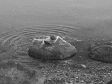 a black and white photo of a person laying on a rock in the water