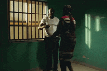 a man and a woman are standing next to each other in front of a window in a jail cell .