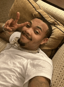 a man in a white shirt is laying on a couch giving the peace sign