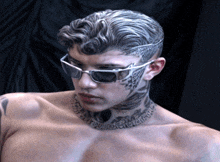 a shirtless man with a tattoo on his face and neck wearing sunglasses