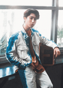 a young man wearing a tie dye jacket is leaning against a window sill