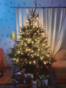 a christmas tree is lit up in a living room with gifts underneath it