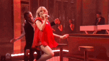 a woman in a red dress is singing into a microphone while a man in a suit is dancing behind her .