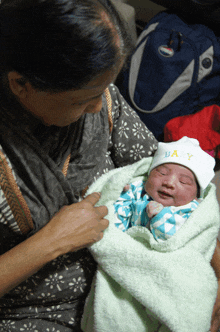 a woman is holding a baby wrapped in a blanket and wearing a baby hat