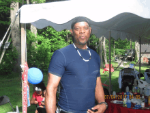 a man in a blue shirt stands in front of a white tent with a photo taken on 07/04/2017