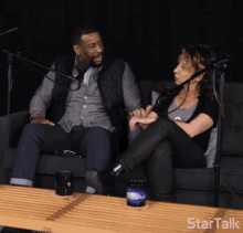 a man and a woman are sitting on a couch in front of a microphone with startalk written on a table