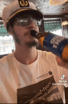 a man wearing a captain 's hat and glasses is drinking from a bottle of beer