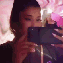 ariana grande is taking a selfie with her phone in front of a pink wall .